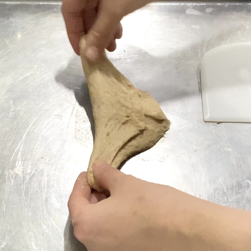two hands stretching out a small piece of dough to shape it into a ball